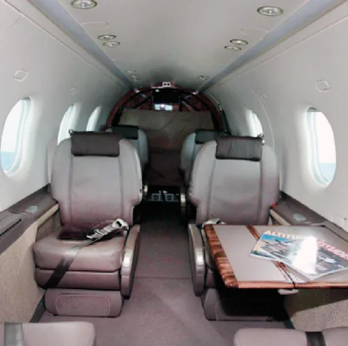 The interior cabin of an aircraft features grey leather seats, a fold-out table with magazines, and overhead lighting.