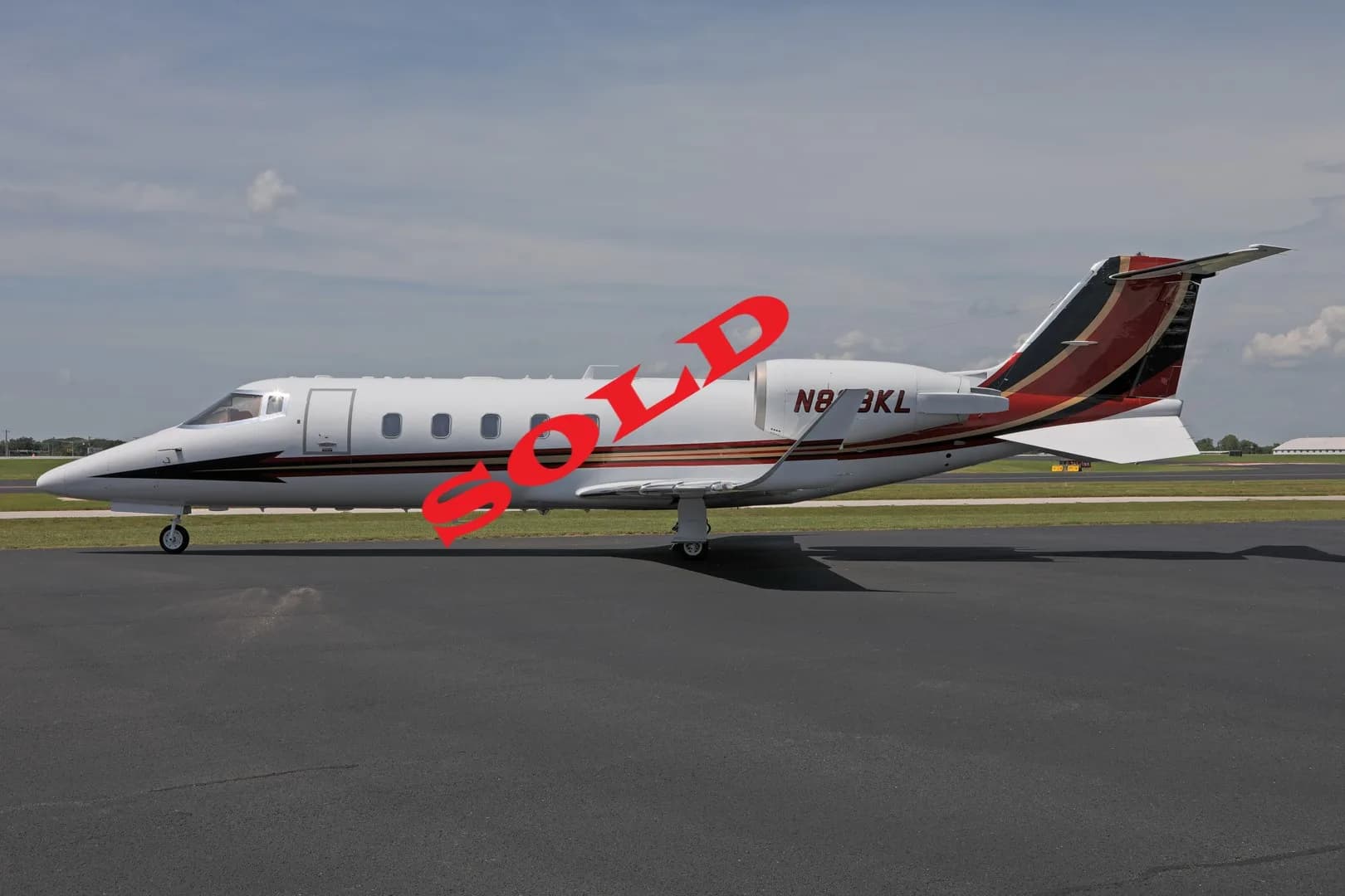 A white business jet with red and black tail accents, registration N873KL, parked on an asphalt runway under a partly cloudy sky.