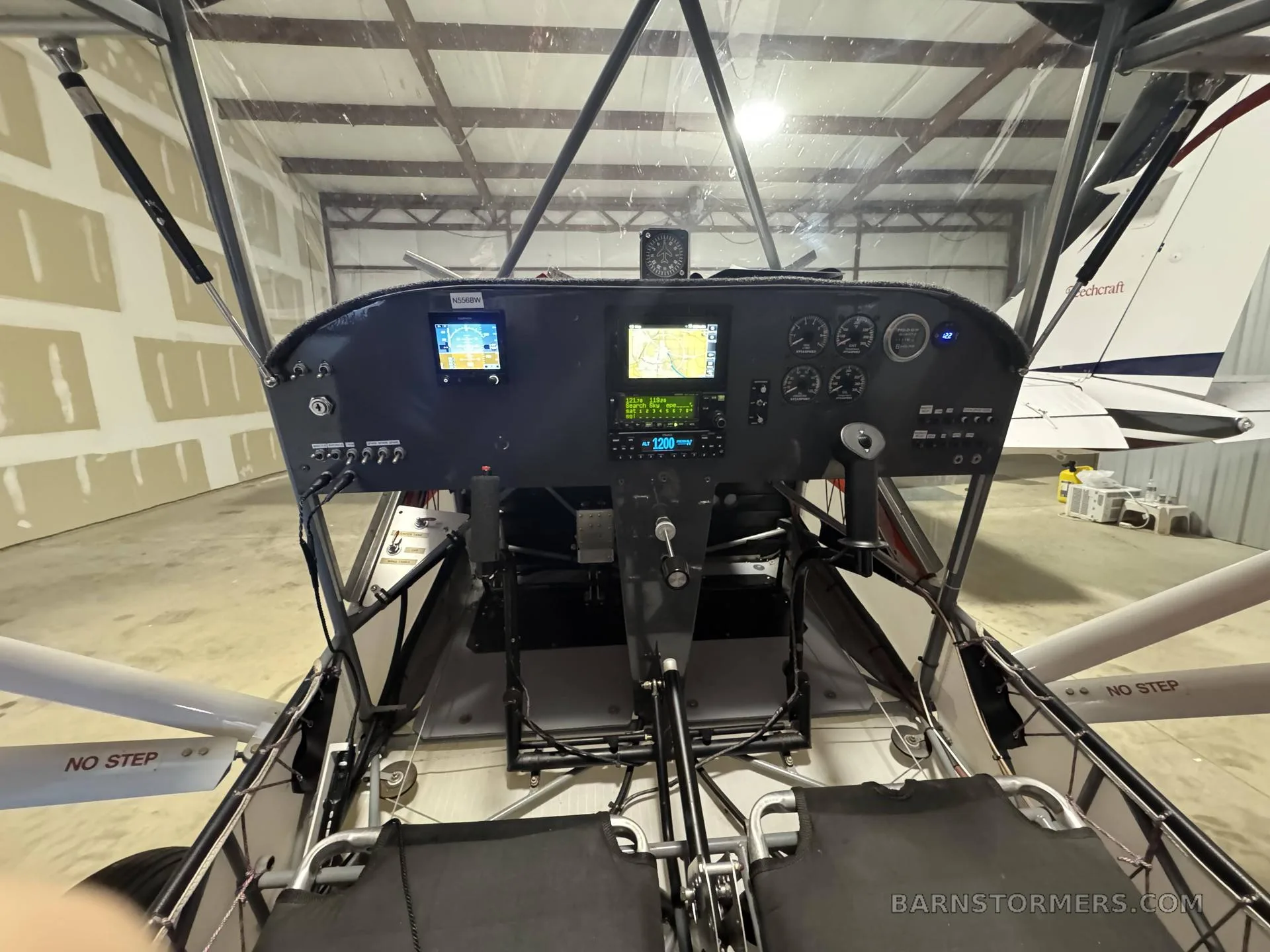 The cockpit of a light sport aircraft, showing the instrument panel, controls, and two seats inside a hangar.