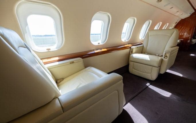 Aircraft cabin interior with cream-colored leather seats and wood paneling.