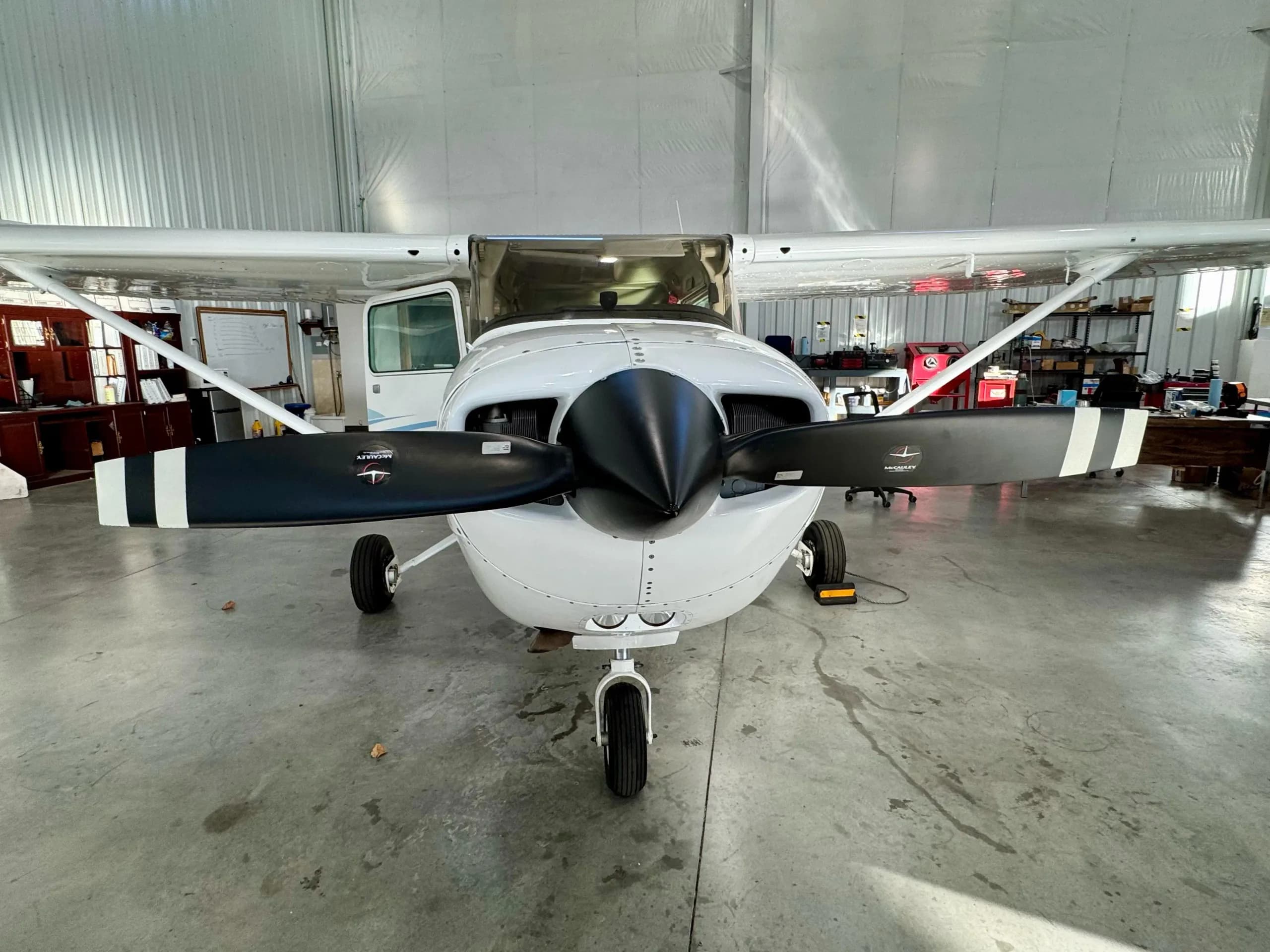 A front view of a white Cessna 172 Hawk XP aircraft with a black propeller, parked in a hangar.