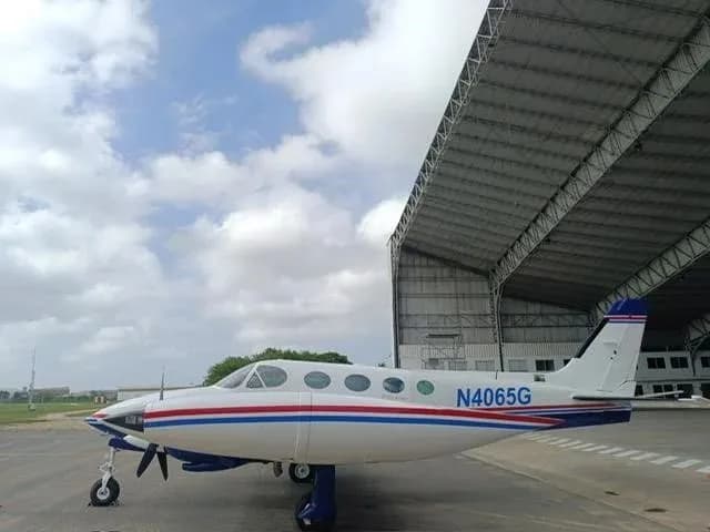 A side view of a white and blue Cessna 340 twin-engine aircraft with red stripes parked on an airfield.