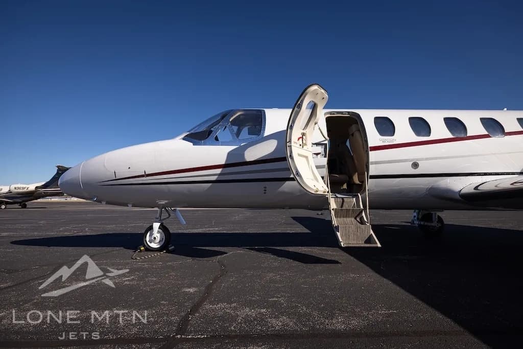 A close-up side view of a white Cessna Citation Bravo jet, tail number N700NR, with its main cabin door open on an airport tarmac.
