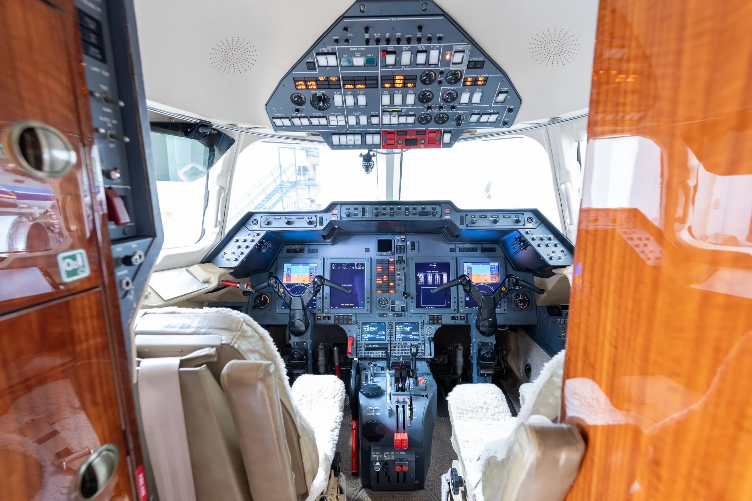 The cockpit of a business jet, seen from the cabin entrance, with multiple screens and controls.