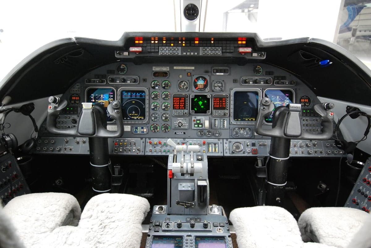 The cockpit of a business jet, showing the instrument panel with multiple displays, yokes, and throttle quadrant.