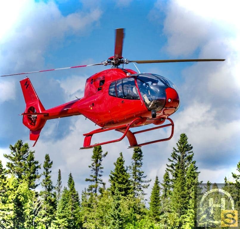 A red Airbus helicopter flies over a forest.