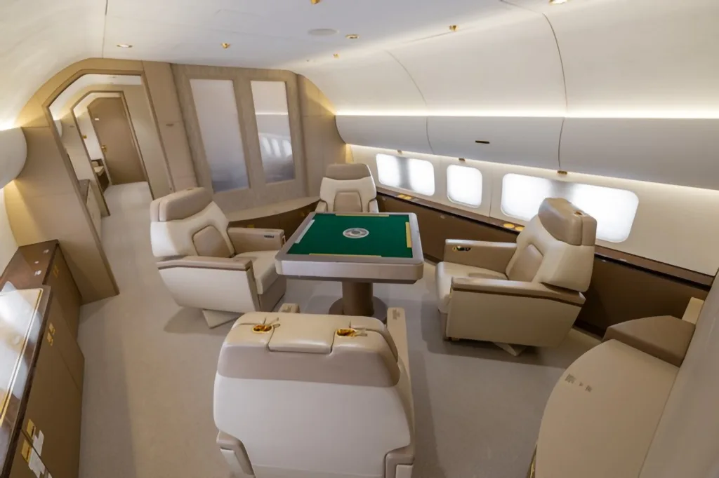 A private section of an aircraft cabin featuring four beige leather seats around a green-topped game table.