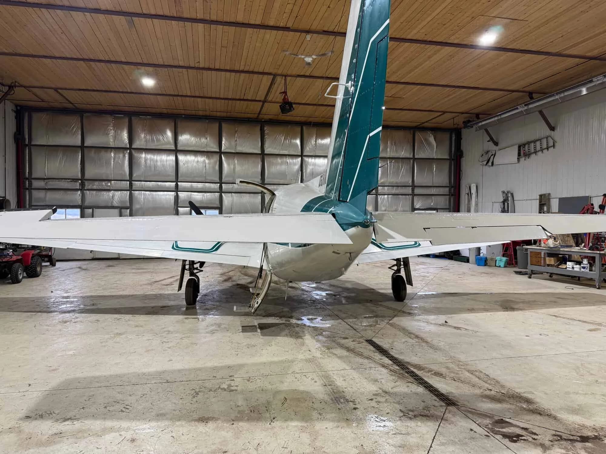 Rear view of a white and green twin-engine aircraft, registration C-GQRM, parked in a hangar.