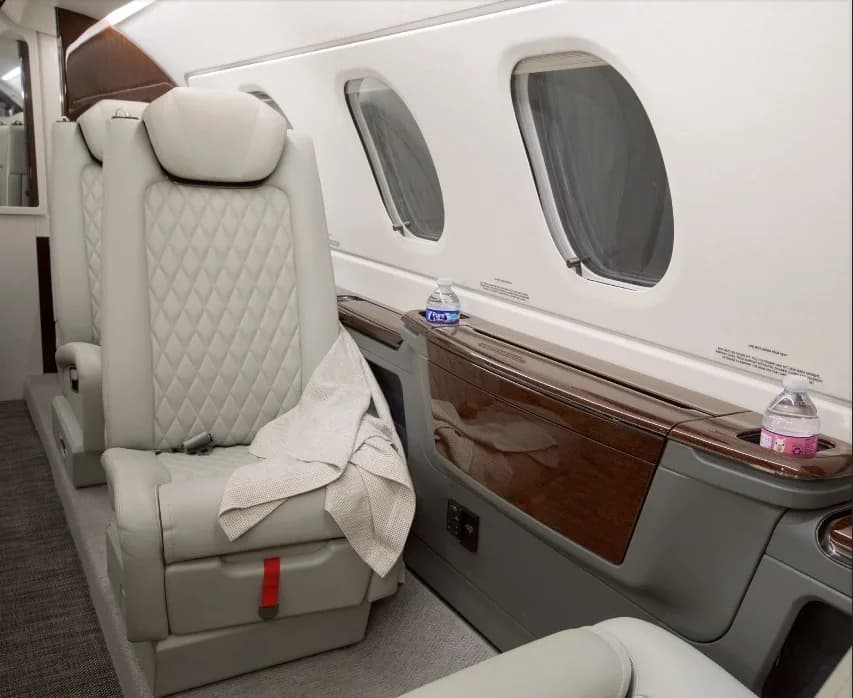 A close-up of the light-colored quilted leather seats and large windows in the aircraft cabin.