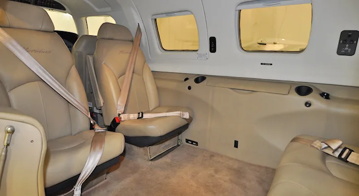 The tan leather interior of an aircraft cabin, showing two rear passenger seats with seatbelts.
