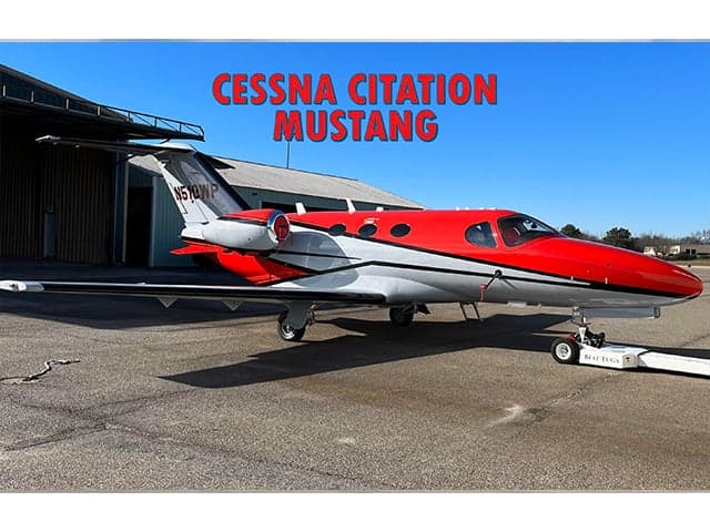 A Cessna Citation Mustang aircraft with a red and white paint scheme is parked on the tarmac.