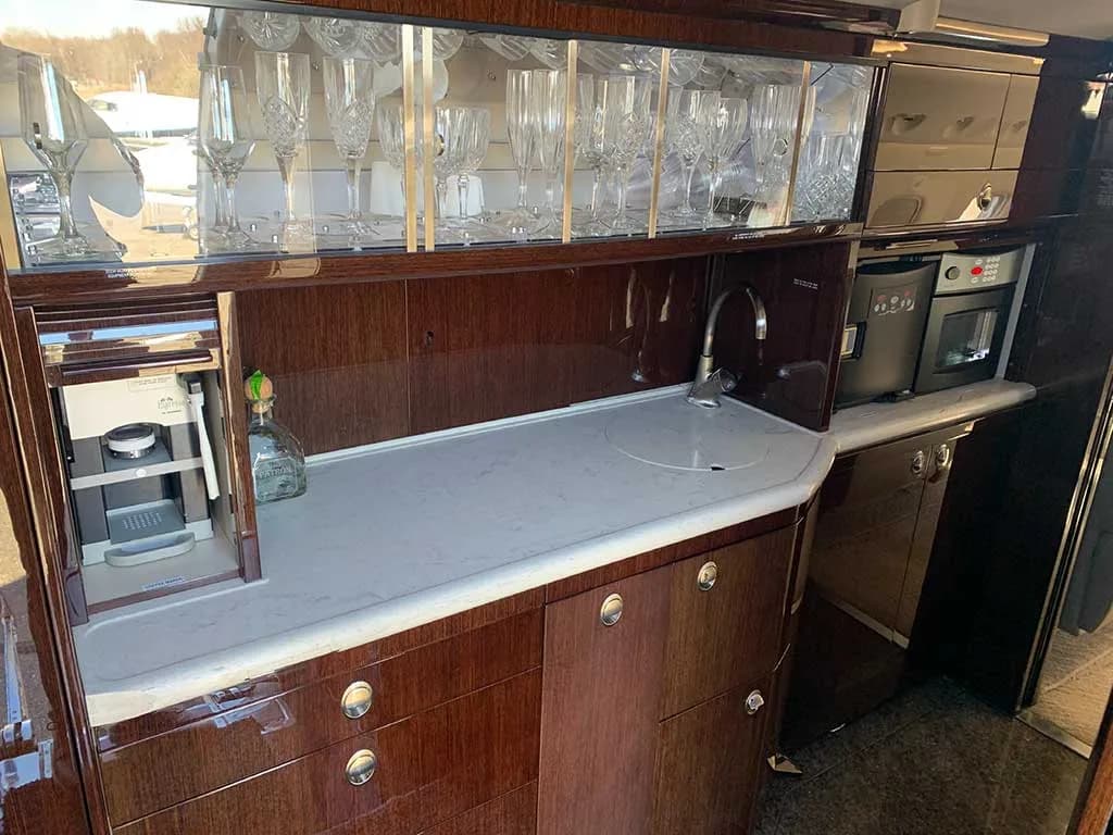 The aircraft's galley area with dark wood cabinetry, a light countertop, sink, and glassware storage.