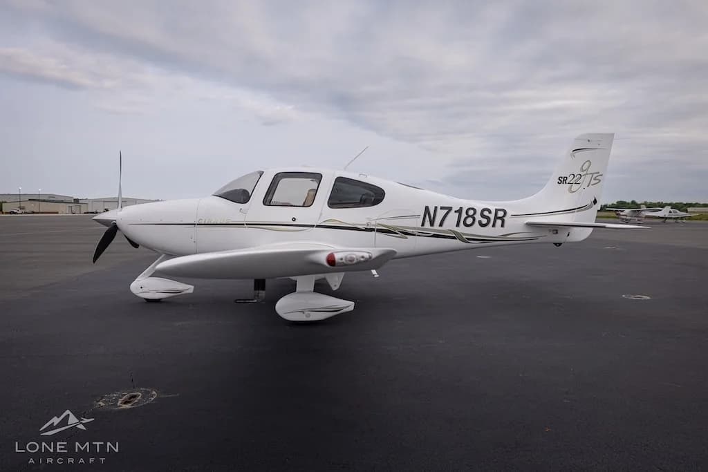 Side view of a white Cirrus SR22T aircraft with black and gold accents parked on an asphalt tarmac.