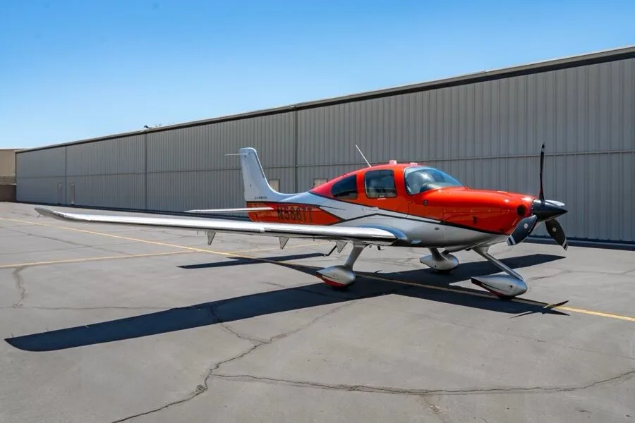 Three-quarter front view of a red and silver Cirrus SR22T aircraft (N566TT) parked on an airfield.