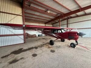 A red Cubcrafters aircraft is parked in a hangar.
