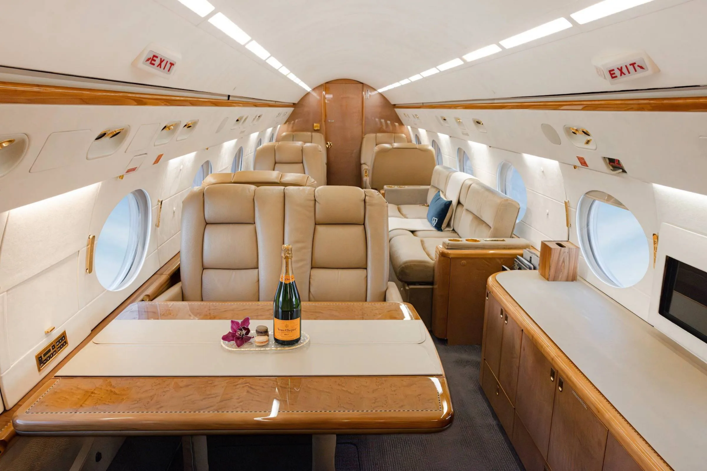 A private jet cabin interior featuring a dining table with champagne and orchids, surrounded by tan leather seating.