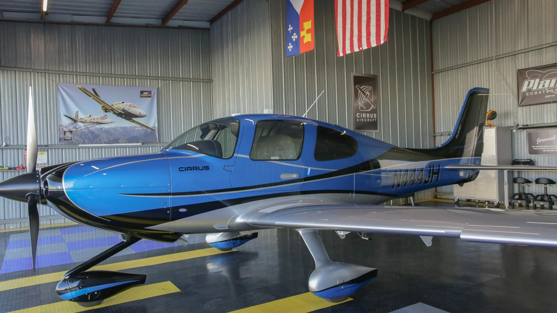 A close-up side view of a blue and silver Cirrus SR22 aircraft with registration N444JH inside a hangar.