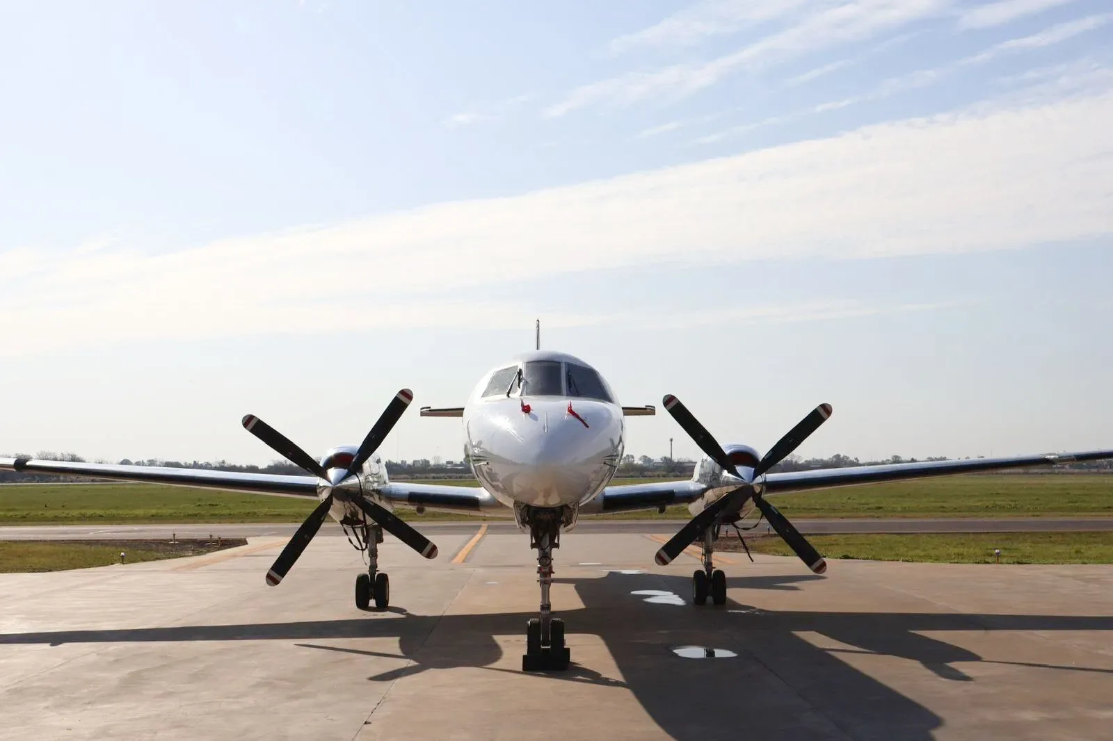 A head-on view of a white turboprop aircraft with two large propellers, parked on an tarmac under a clear sky.