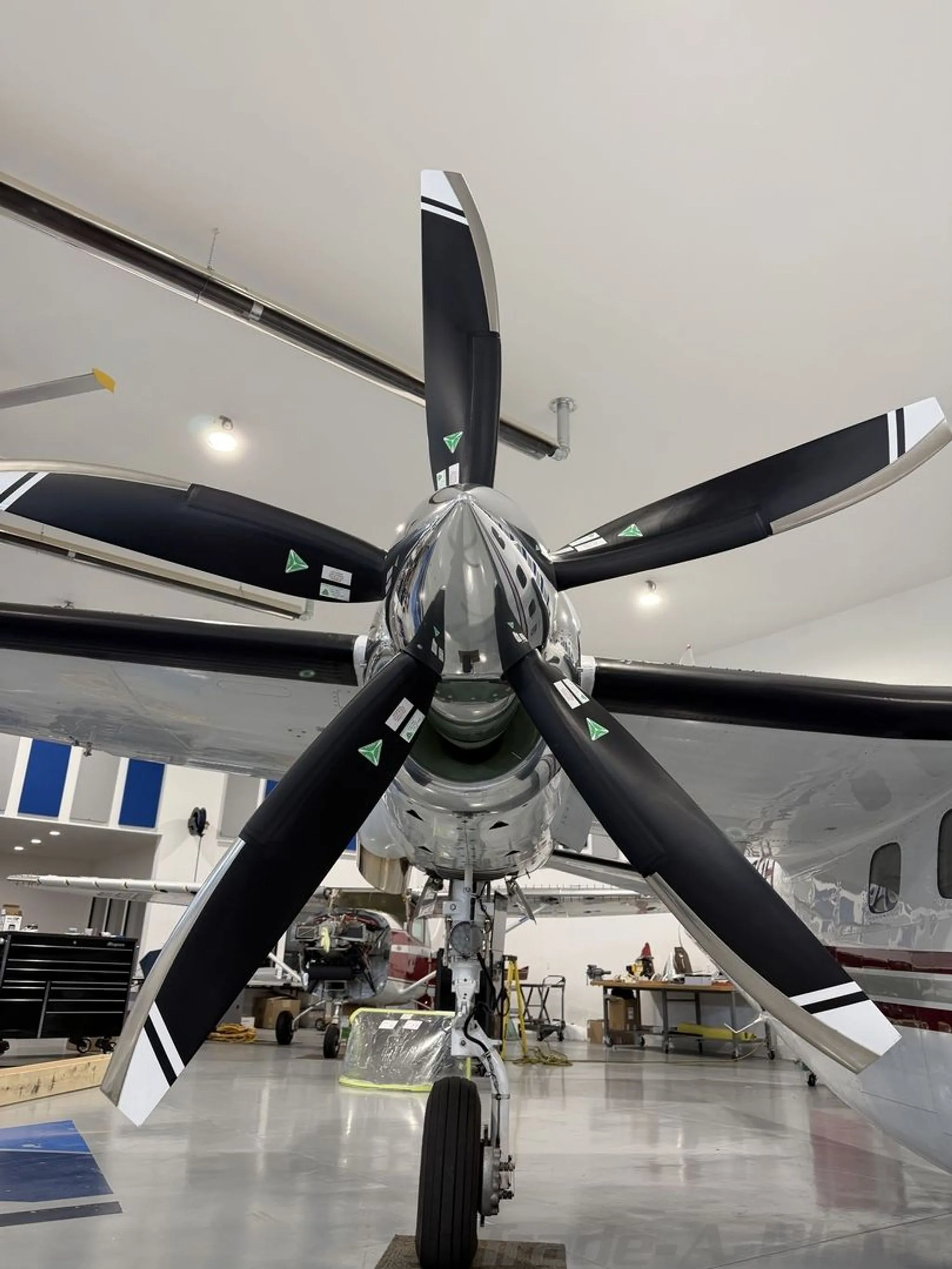 A close-up view of a large black five-bladed propeller with white tips on a turboprop aircraft in a hangar.
