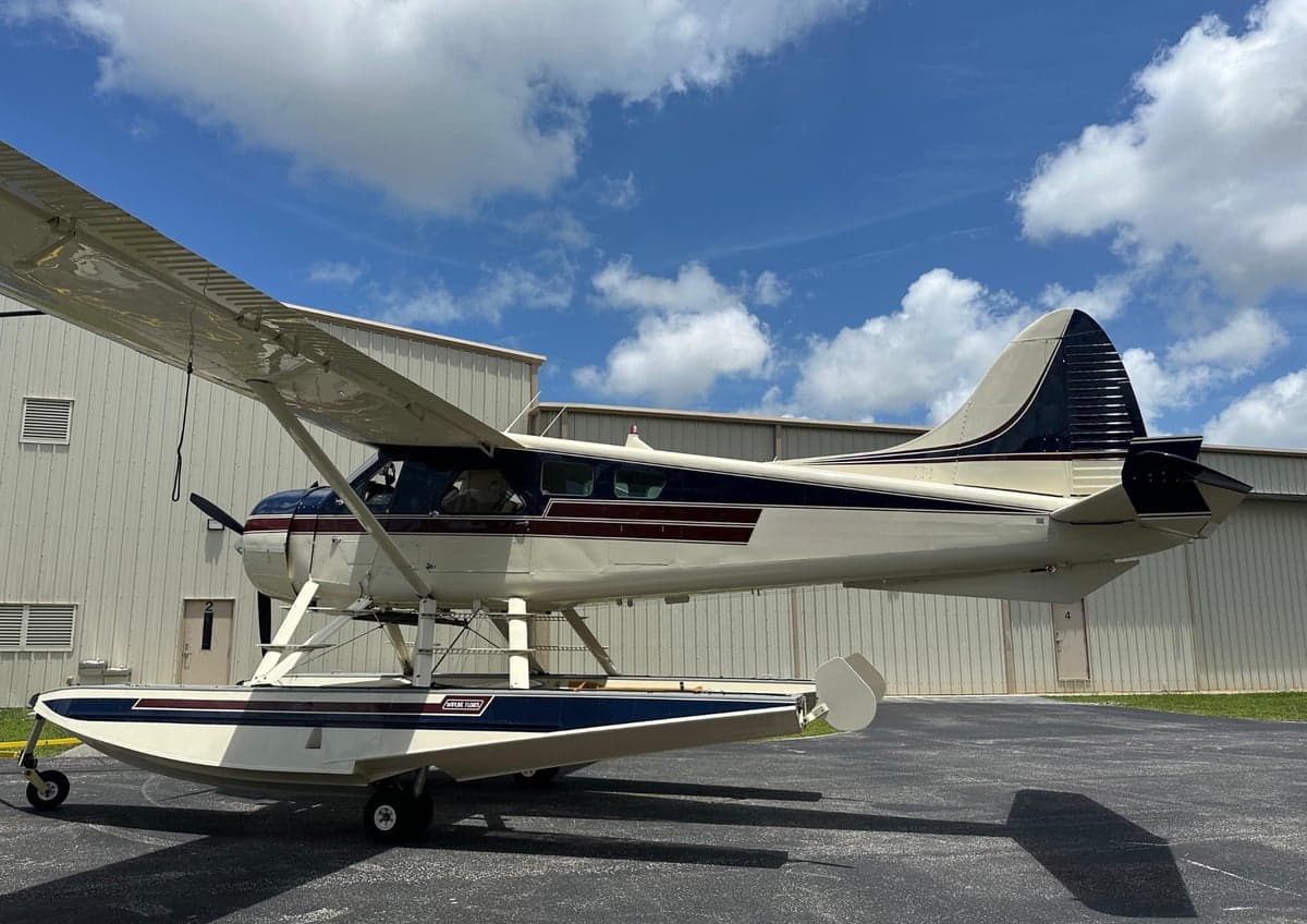Side view of a white and maroon floatplane on the tarmac.