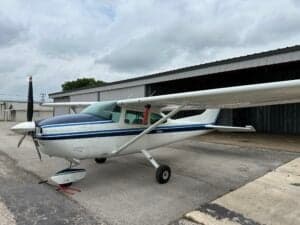 A Cessna aircraft parked outside a hangar with a white and blue paint scheme.