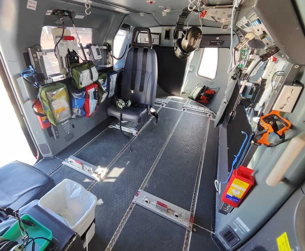 A wide view of the helicopter's interior cabin, showing a utility configuration with floor tracks and various bags and equipment.