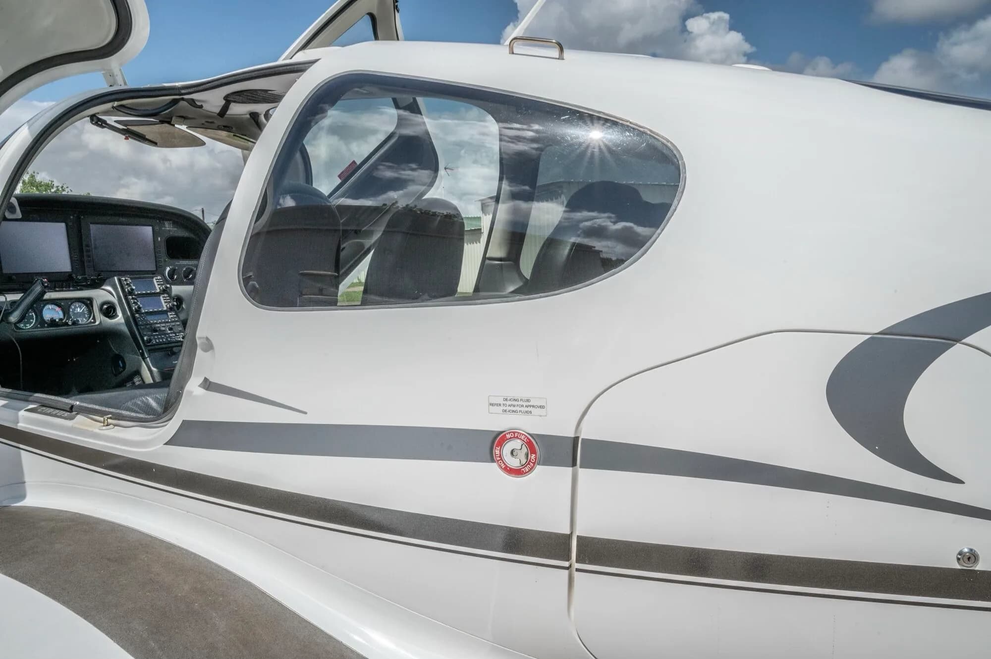 A close-up of the side of the white Cirrus SR22 GTS fuselage with the door open, showing the interior and a reflection of the sky.