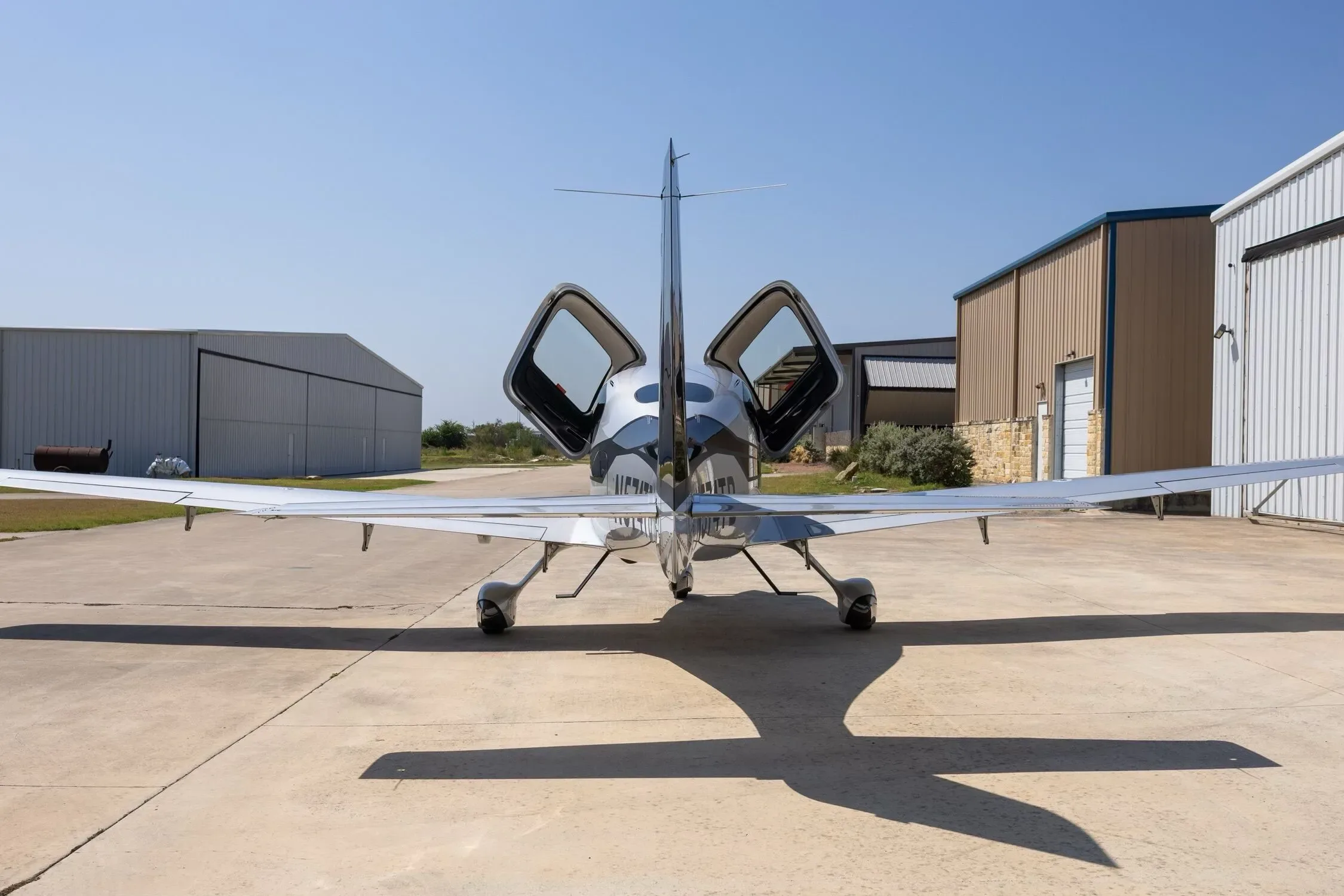 A rear view of the silver and black Cirrus SR22 aircraft, registration N574TB, with its doors open, parked on an airfield.
