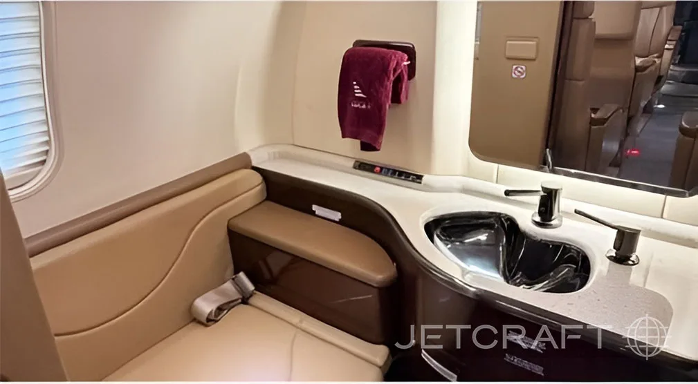 The lavatory of a business jet with a sink, mirror, and a small bench seat.
