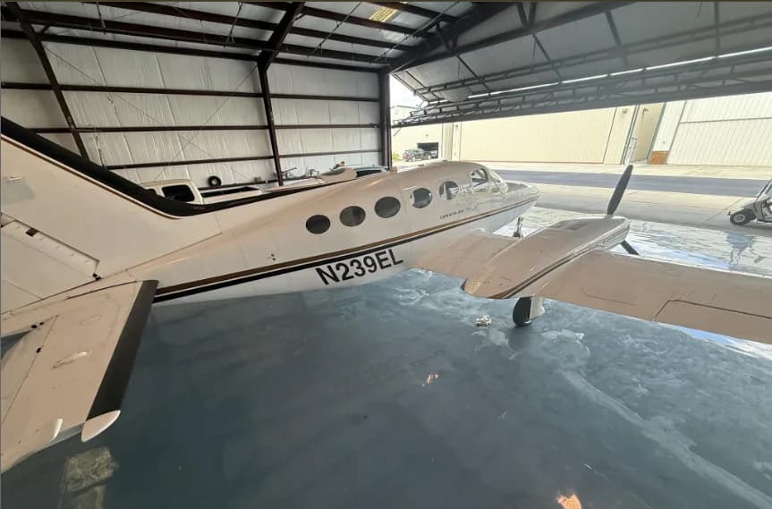 A side view of the white Cessna 414 aircraft with gold and black stripes and registration N239EL, parked in a hangar.