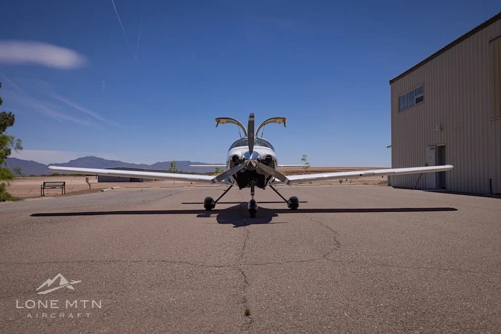 A head-on view of a white and black single-engine aircraft, N65035, with its gull-wing doors open, parked on an airport ramp.