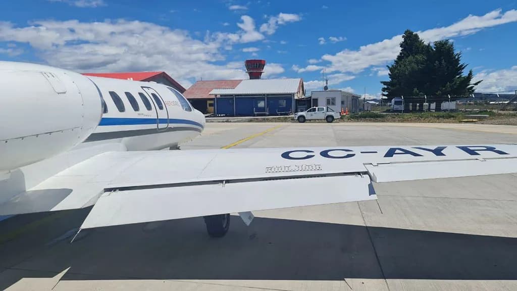 The white wing and tail of a business jet with registration CC-AYR, parked on an airfield with an airport control tower in the background.