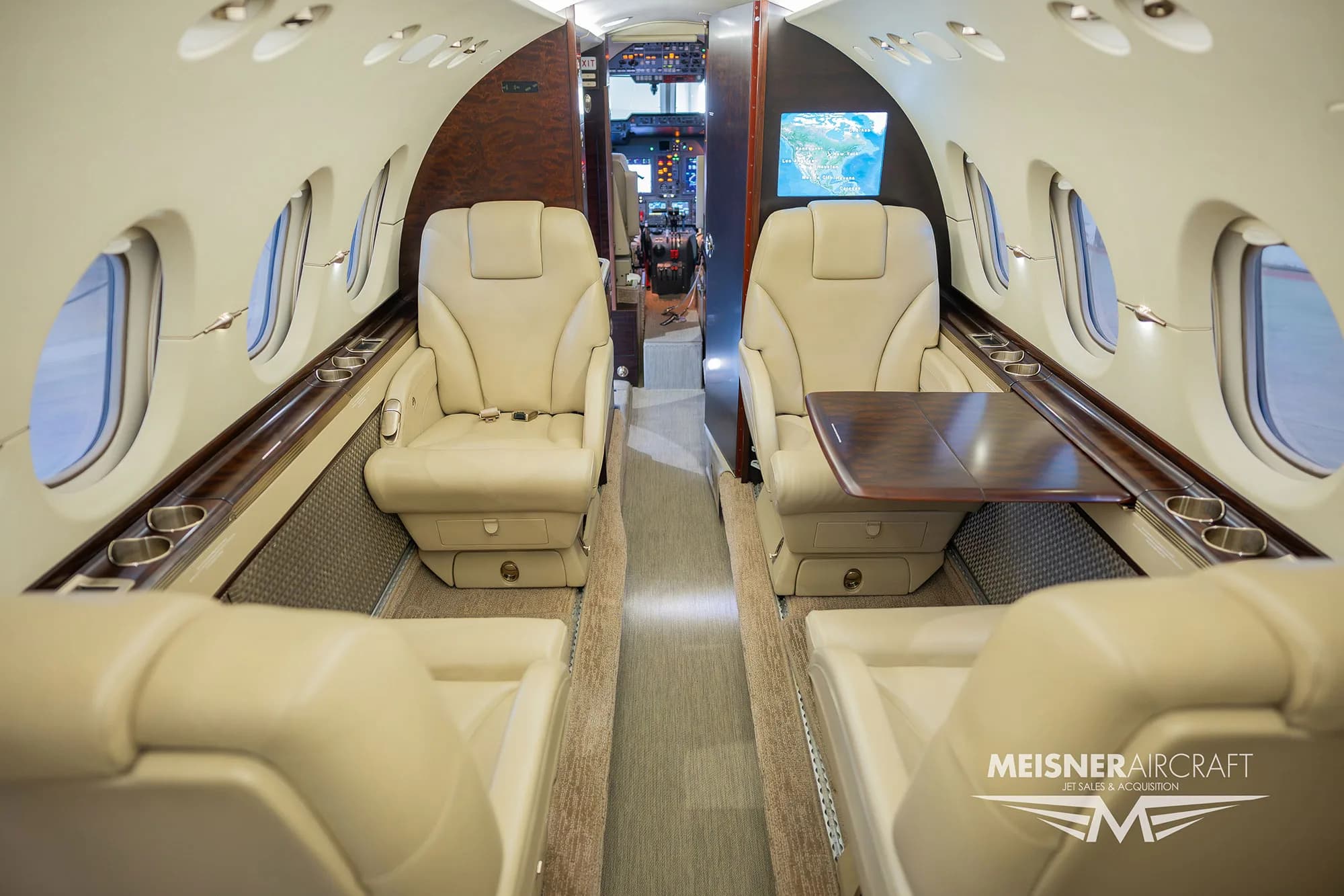 The luxurious cabin interior of a business jet, featuring beige leather seats and a wooden table.
