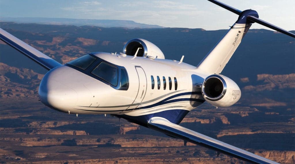 A close-up of a Citation CJ4 in flight with a blue and white paint scheme.