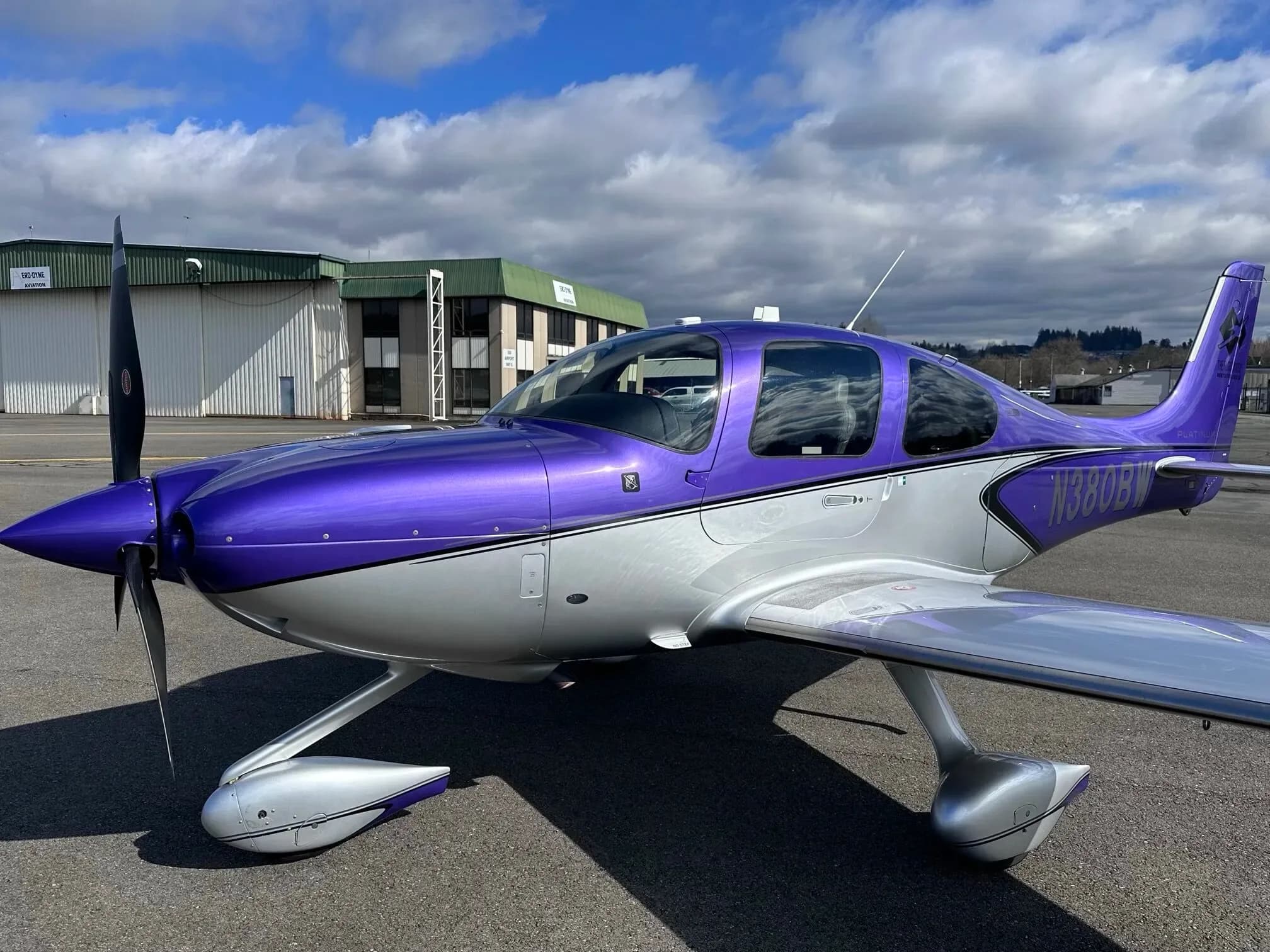A front three-quarter view of the purple and silver Cirrus SR22 aircraft, N380BW, parked on an airport tarmac.