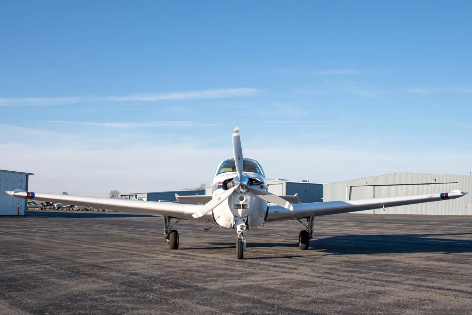 Front view of a white Beechcraft Bonanza N2261L with a single propeller on an airfield.