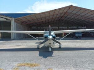 Front view of a Cessna aircraft with blue and white paint scheme, parked on the tarmac in front of a hangar.