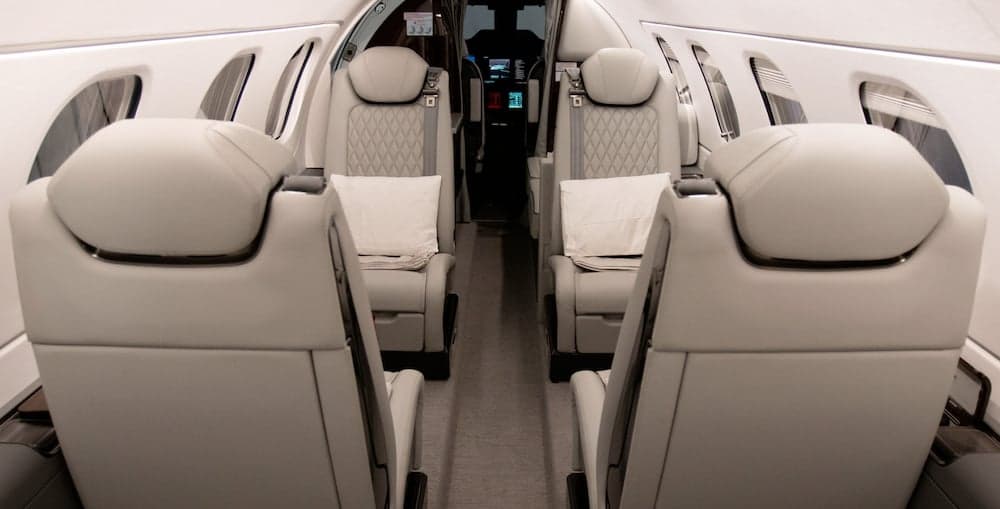 Aircraft interior showing four leather seats with white pillows.