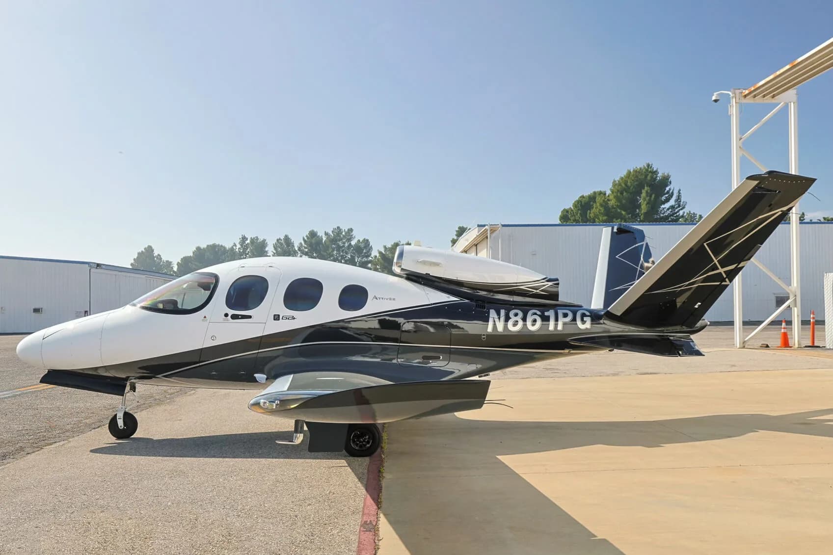 A Cirrus Vision Jet (N861PG) in white, black, and grey paint scheme parked on an tarmac with trees in the background.