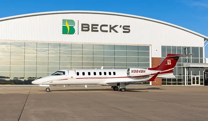 White jet with red stripes parked in front of a Beck's hangar.