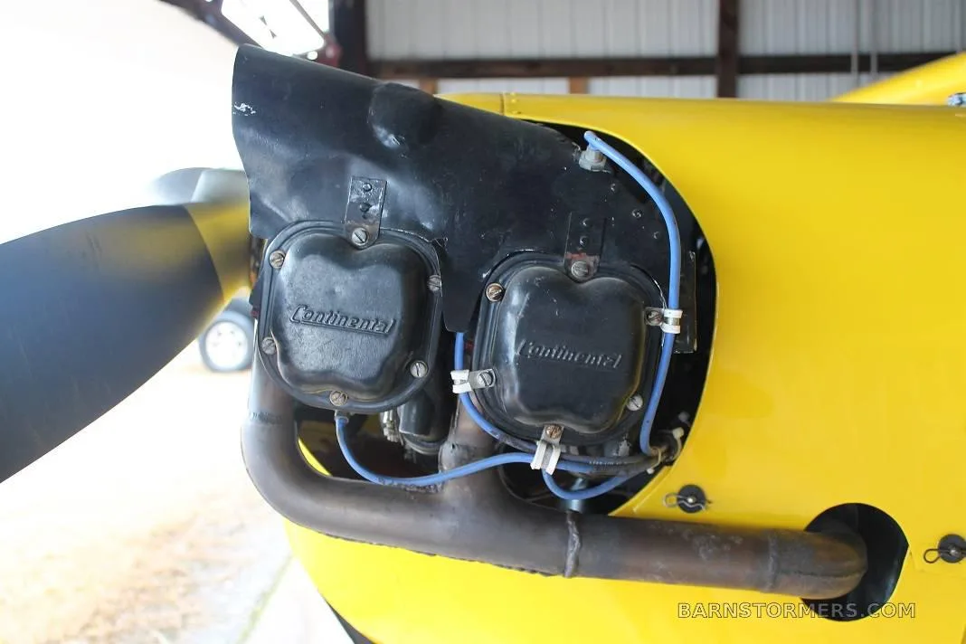A close-up view of the Continental engine cylinders and exhaust manifold on a yellow aircraft.