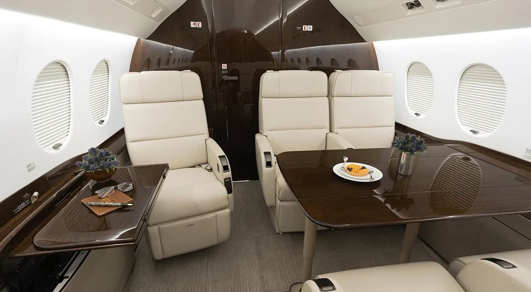 The aircraft interior features cream-colored leather seats and wood tables with decorative items.