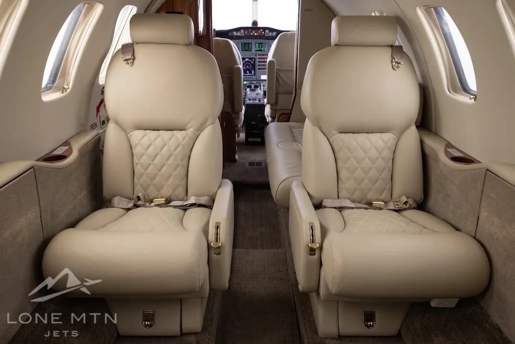 Two rows of light-colored quilted leather passenger seats in the cabin of a business jet, looking towards the cockpit.