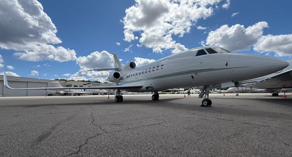 A Falcon aircraft is parked on the tarmac under a partly cloudy sky.