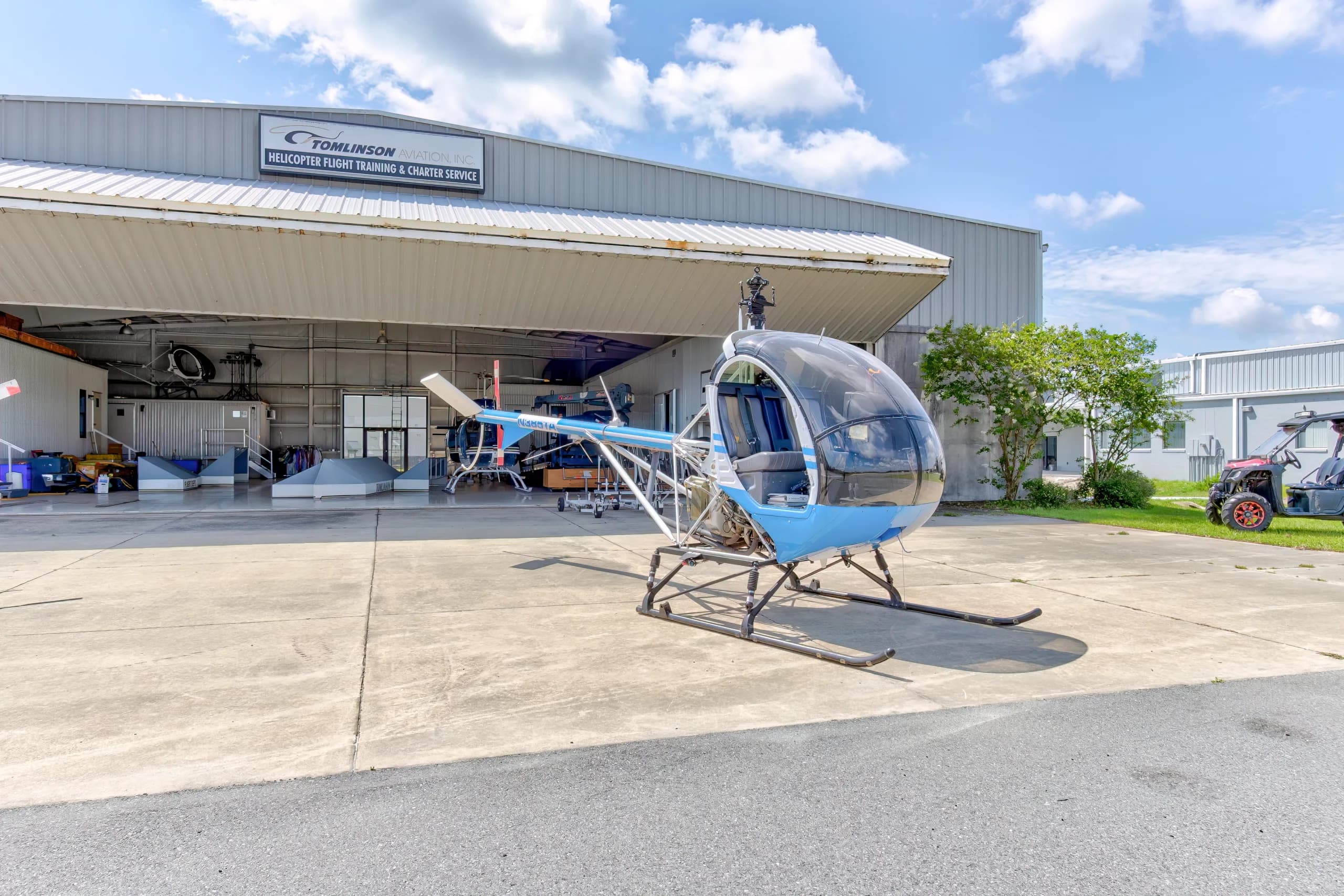 A blue and white Schweizer 300CBi helicopter, N385TA, parked on an airfield tarmac in front of a hangar.