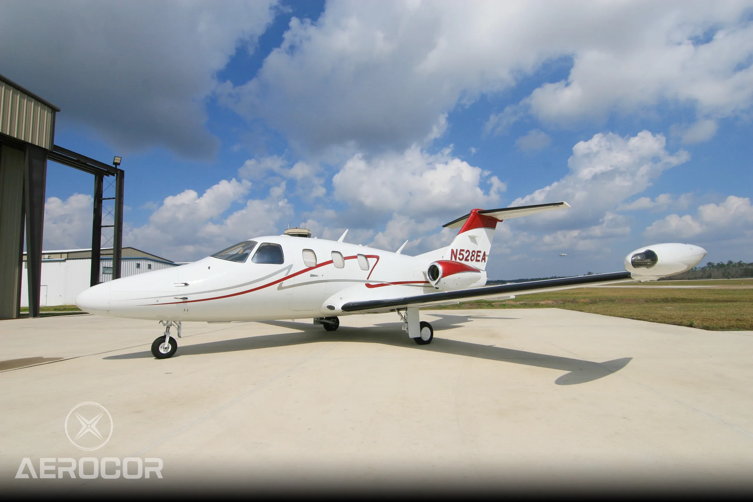 A white Eclipse 500 jet with red and grey stripes, registration N528EA, parked on an airport tarmac next to a hangar.