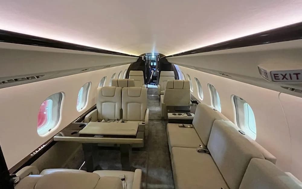 A wide-angle view of a private jet cabin with cream seating, including a sofa and individual chairs, and a table.