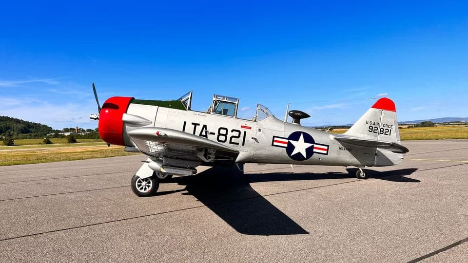 A T-6 Texan aircraft with a silver and red paint scheme parked on the tarmac.