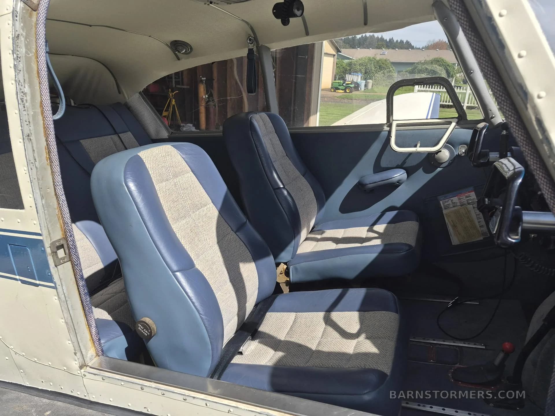 The interior cabin of a small aircraft, showing blue and patterned fabric seats and a view outside the door.