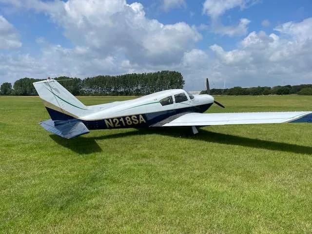 Rear-side view of the N218SA single-engine aircraft, painted white and blue, parked on a grassy field.